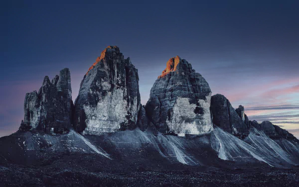 HD desktop wallpaper depicting the rugged peaks of Tre Cime di Lavaredo under a clear twilight sky, showcasing the natural beauty of this iconic mountain formation.
