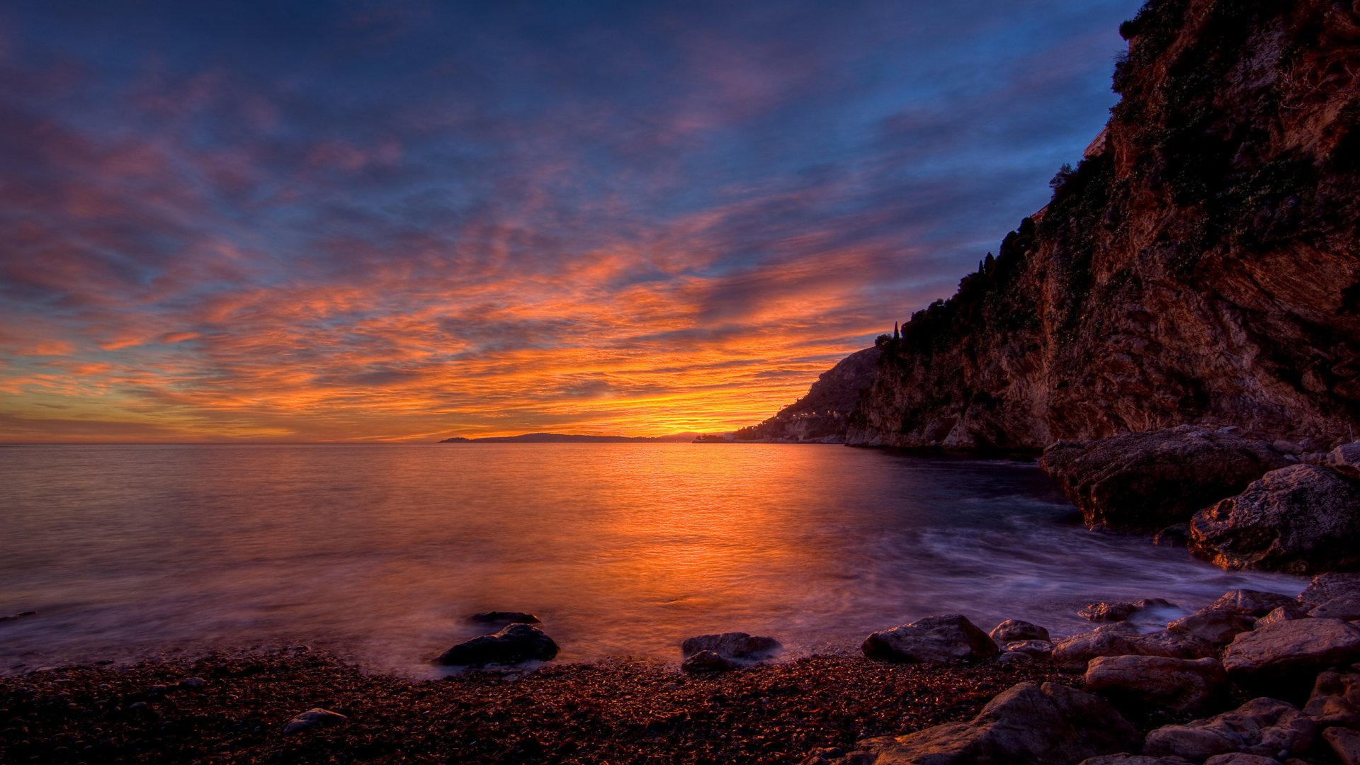A stunning sunset over the ocean, with vibrant hues reflecting on the water and a rugged coastline in the foreground, creating a serene natural scene for your HD desktop wallpaper.