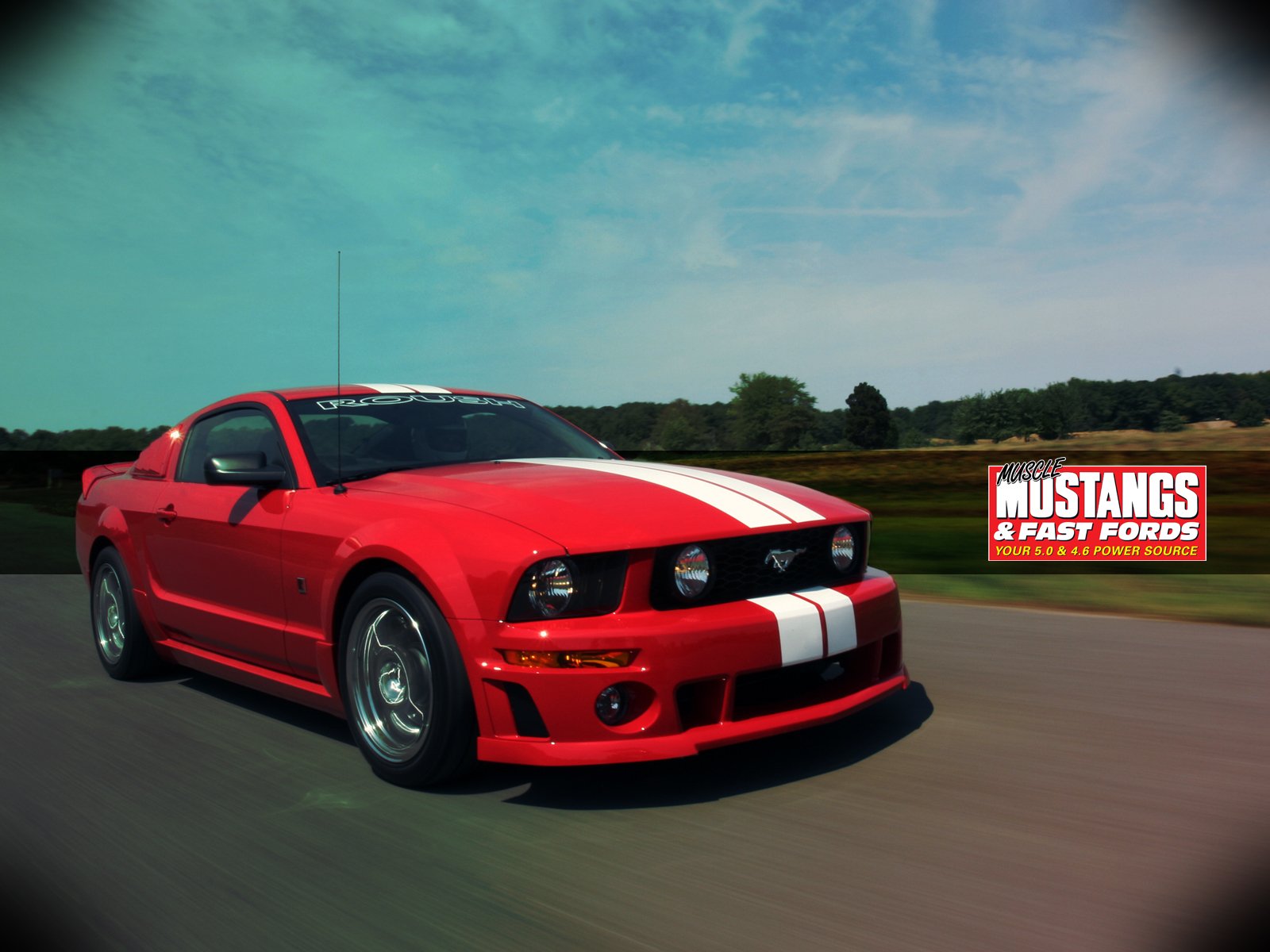 HD desktop wallpaper of a red Ford Mustang with white racing stripes driving on a road, featuring clear skies and a Mustangs & Fast Fords logo on the right side.