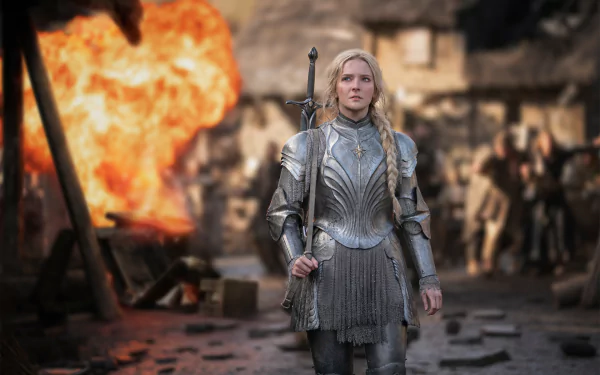 Galadriel, portrayed by Morfydd Clark, stands resolute in armor amid chaos, surrounded by flames in a scene from the TV show The Lord of the Rings: The Rings of Power.
