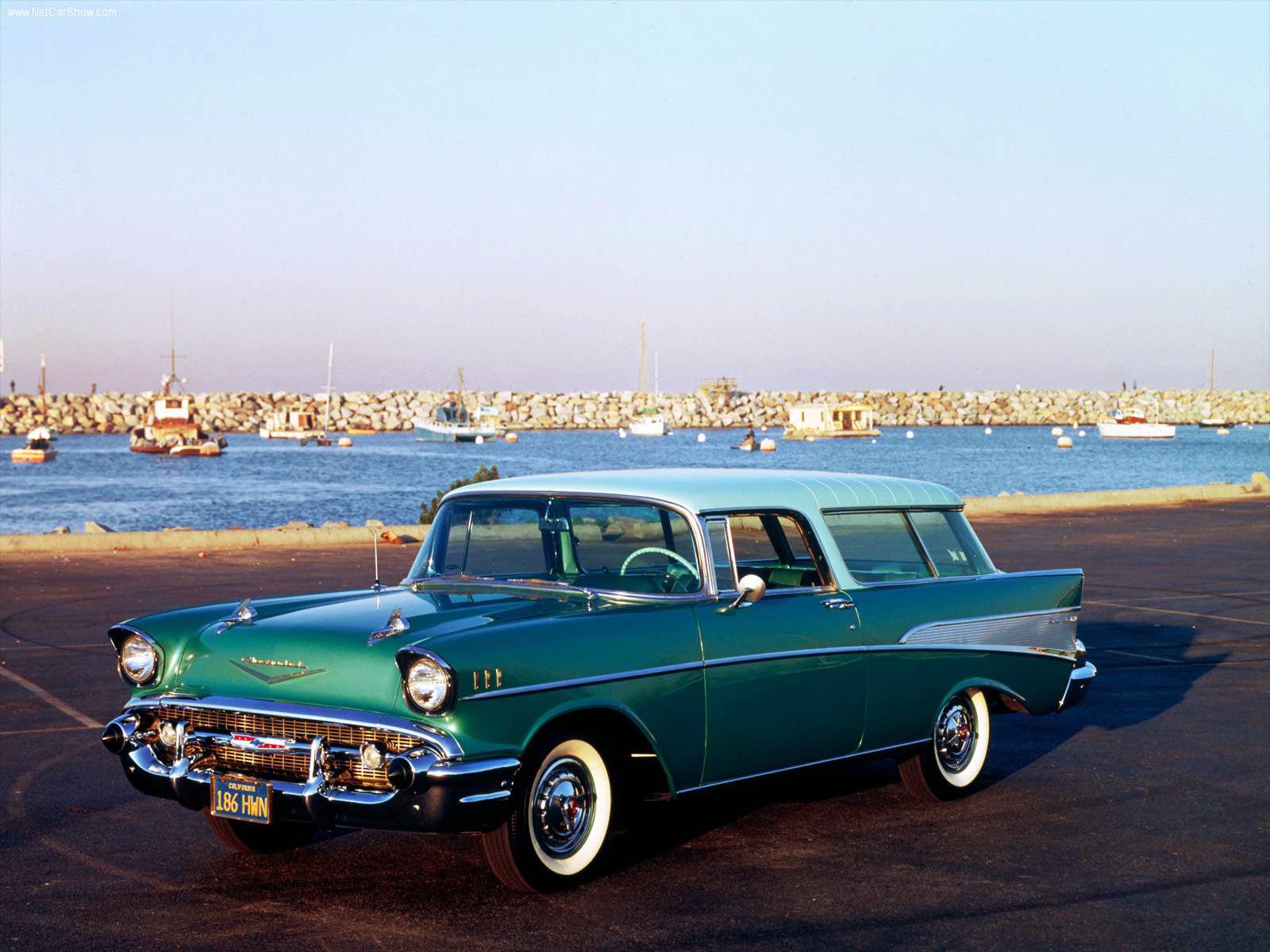 HD desktop wallpaper featuring a classic green Chevrolet Nomad parked by a waterfront with boats in the background under a clear sky.