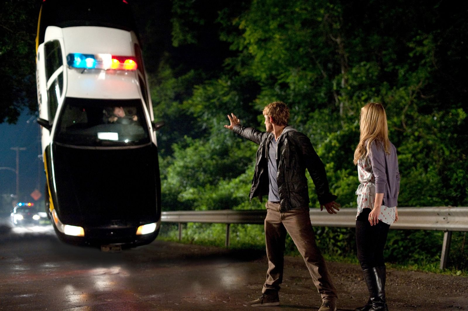 A scene from the movie *I Am Number Four*, featuring a character using telekinesis to levitate a police car, while another character watches, set against a nighttime forest backdrop.