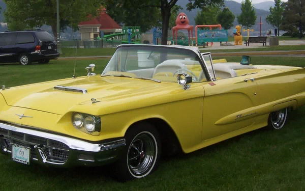 HD PC desktop wallpaper featuring a classic yellow Ford Thunderbird convertible parked on grass in a park with playground equipment in the background.