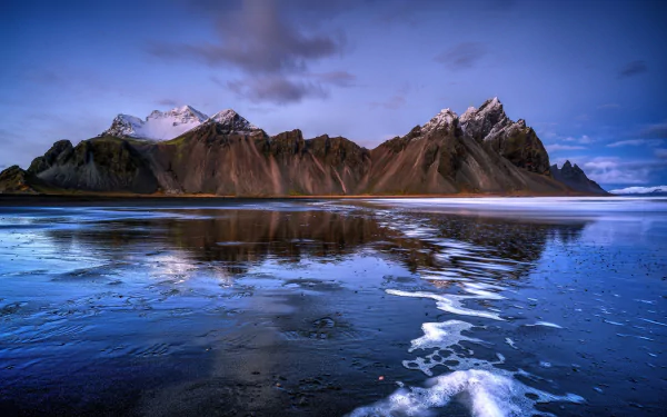 HD desktop wallpaper of Iceland’s Vestrahorn mountain range, showcasing rugged peaks reflected in calm coastal waters under a twilight sky.