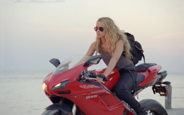A woman with long hair and sunglasses sits confidently on a red motorcycle against a serene ocean background, inspired by the movie I Am Number Four.