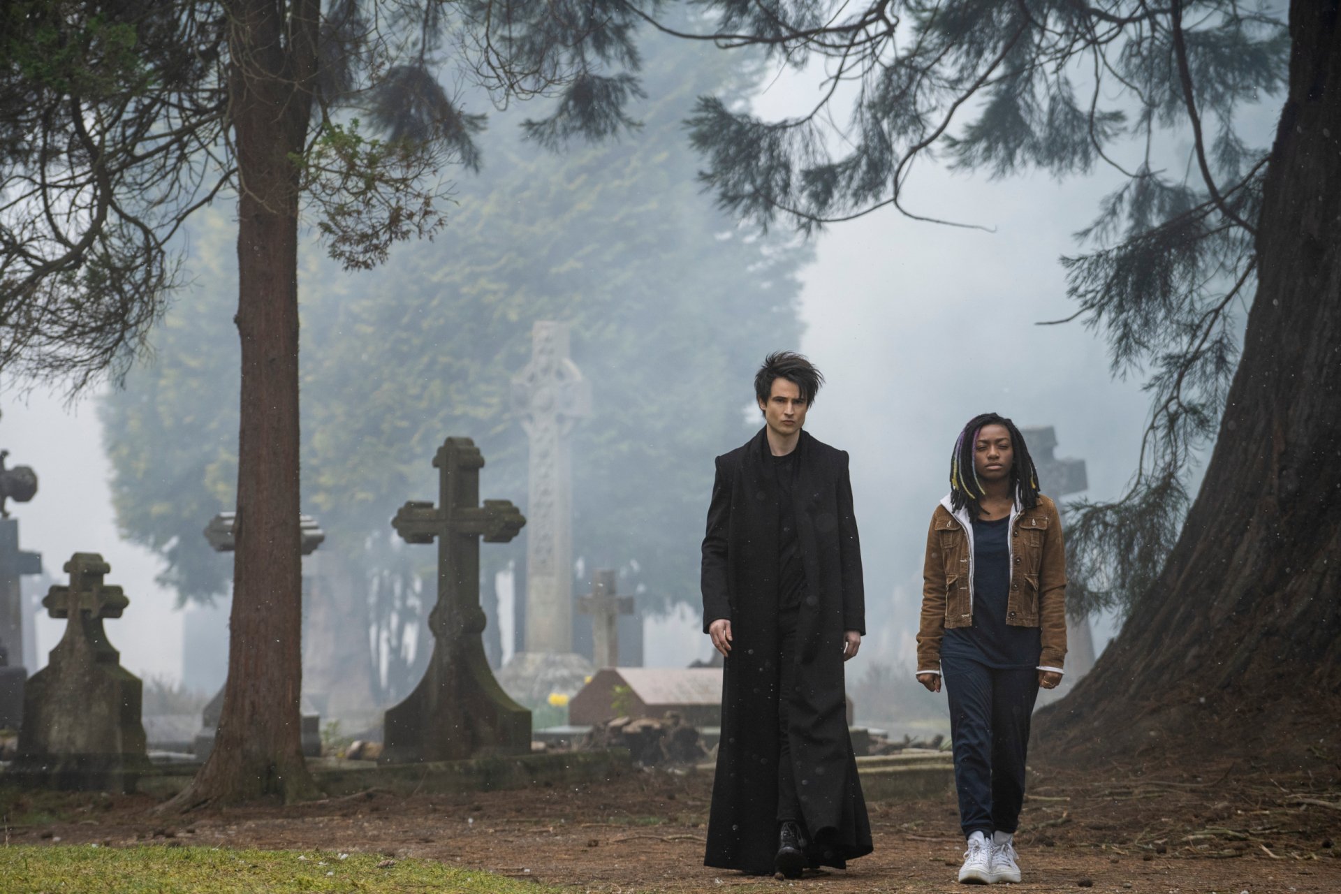 2K Quad HD PC desktop wallpaper from TV show The Sandman: two figures walk through a foggy cemetery among crosses and tall trees.