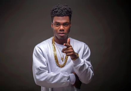 Stylish HD desktop wallpaper featuring a person pointing at the camera, wearing a white shirt and gold chains, with a grey background for a sophisticated look.