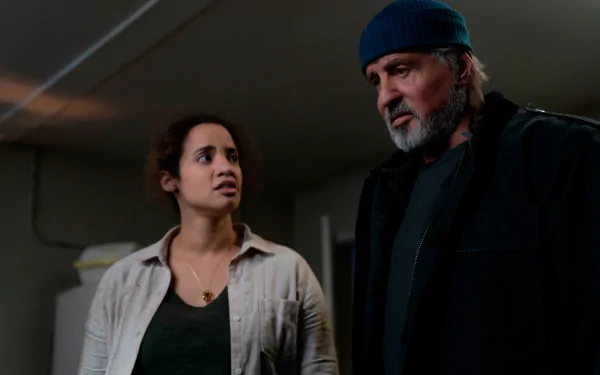 Two characters from the movie Samaritan — an older bearded man in a beanie and a concerned young woman in a dim interior; 2K Quad HD PC desktop wallpaper/background.