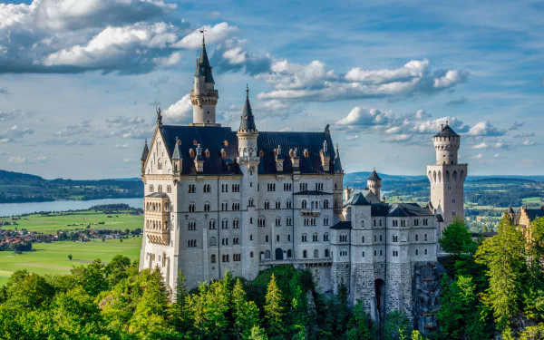 5K Ultra HD PC desktop background: Neuschwanstein Castle, a man-made 19th-century Bavarian palace in Germany perched above green forests under a bright blue sky.