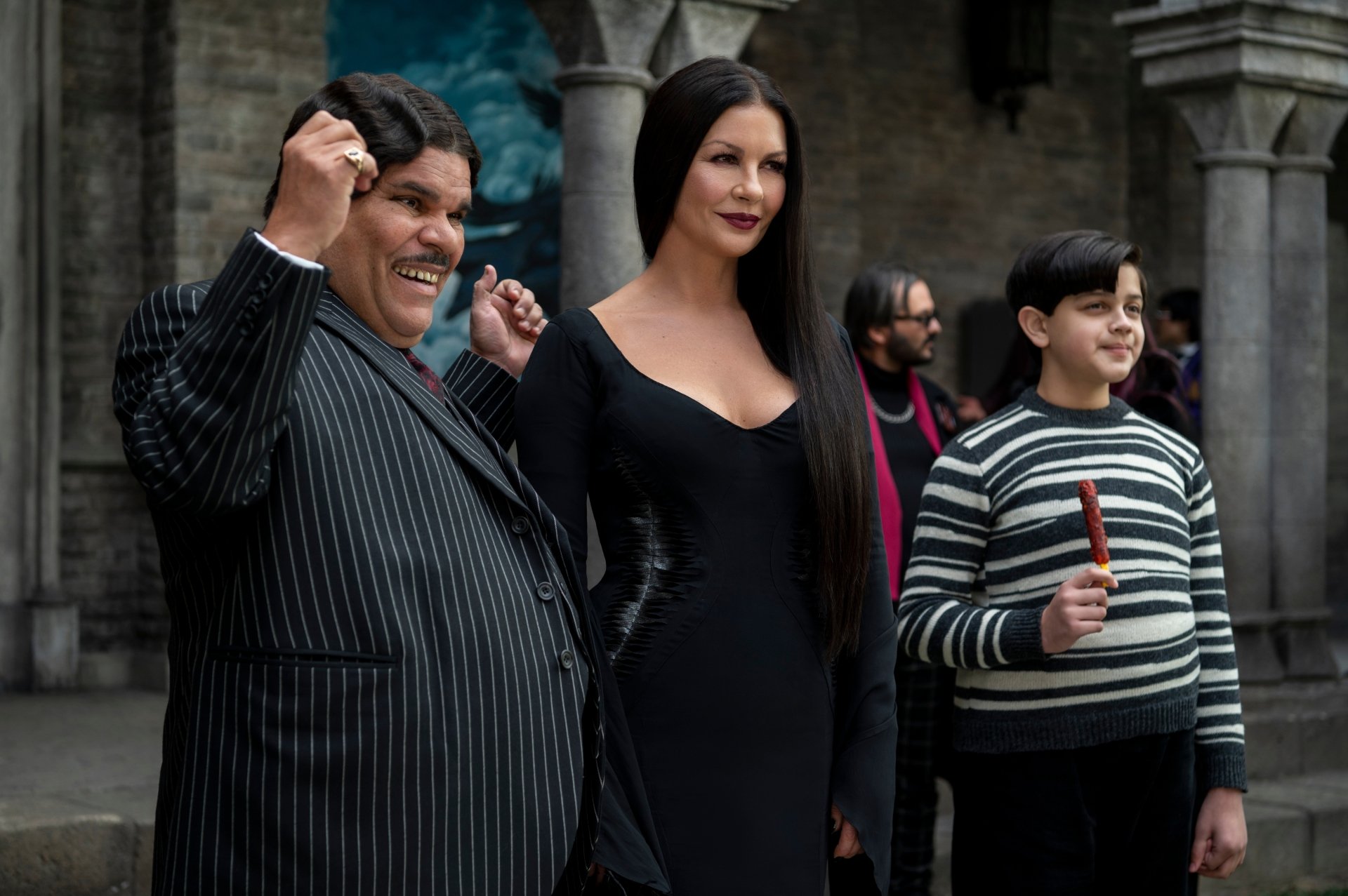 HD desktop wallpaper featuring Luis Guzman as Gomez Addams, Catherine Zeta-Jones as Morticia Addams, and a young boy from the TV show Wednesday.