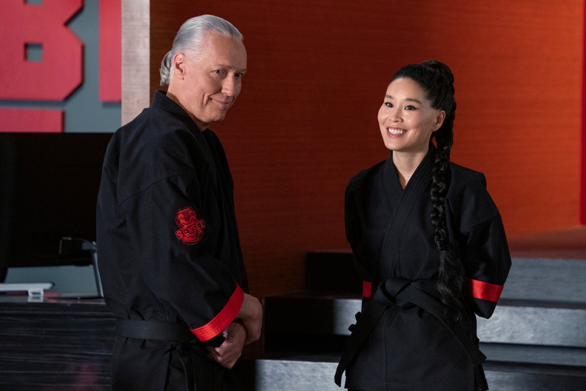 HD PC desktop wallpaper featuring two characters from the TV show Cobra Kai dressed in black martial arts uniforms against a red and black background.
