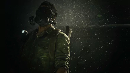 HD PC desktop wallpaper featuring Joel (The Last of Us) from the video game The Last of Us Part I: a rugged survivor in a gas mask with flashlight, rain and dust illuminated against a dark backdrop.