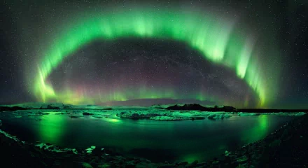 A stunning HD desktop wallpaper featuring the aurora borealis illuminating the night sky over a tranquil lake, with stars twinkling above and their reflections dancing on the water's surface.