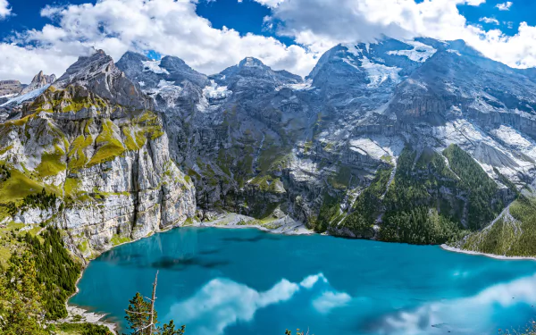 4K Ultra HD wallpaper of Switzerland’s Alps showcasing snow-capped peaks, rocky cliffs, and a vibrant blue lake beneath a partly cloudy sky.