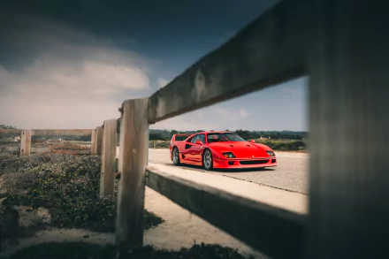 Red Ferrari F40 sports vehicle on a coastal road, framed by a weathered wooden fence — cinematic HD PC desktop wallpaper background.