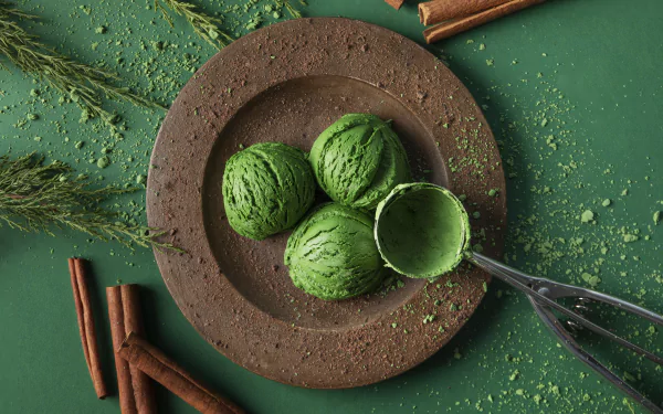 5K Ultra HD PC desktop wallpaper background: three vibrant green matcha ice cream scoops on a rustic brown plate with an ice cream scoop, cinnamon sticks and scattered green powder.