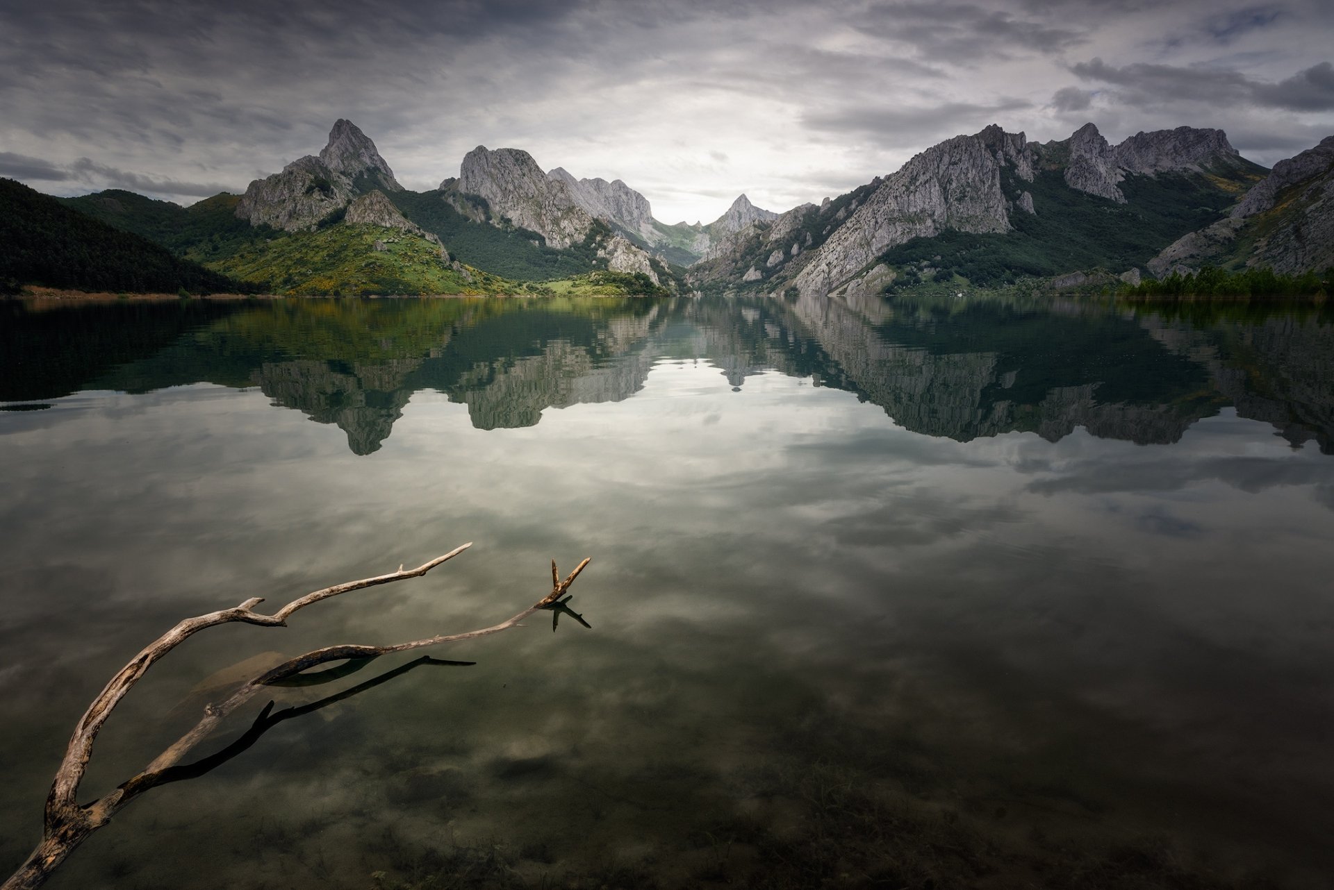 HD PC desktop wallpaper featuring a serene lake reflecting rugged mountains under a cloudy sky, surrounded by natural wilderness.