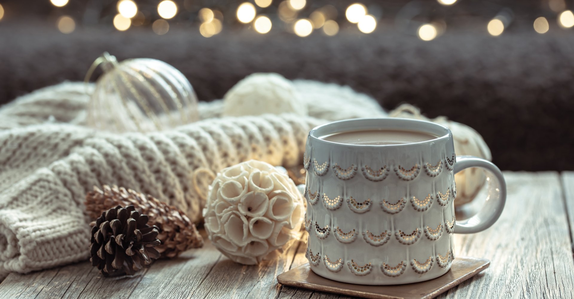 Cozy 4K Ultra HD PC desktop wallpaper featuring a warm mug of coffee surrounded by knitted fabric, decorative ornaments, and soft fairy lights.
