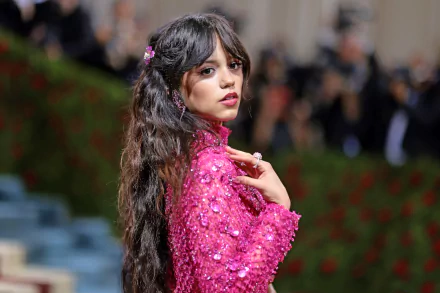 HD desktop wallpaper featuring celebrity Jenna Ortega in a vibrant pink outfit with long wavy hair, posing against a blurred background.