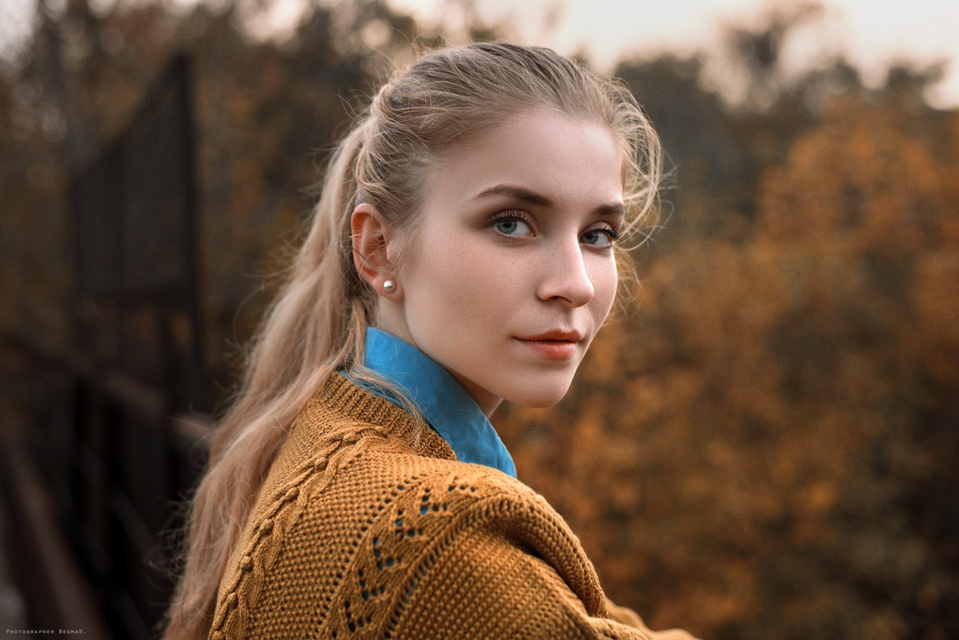 HD PC desktop wallpaper: portrait of a woman model with a blonde ponytail in a mustard knit sweater and blue collar, set against a soft autumnal outdoor background.