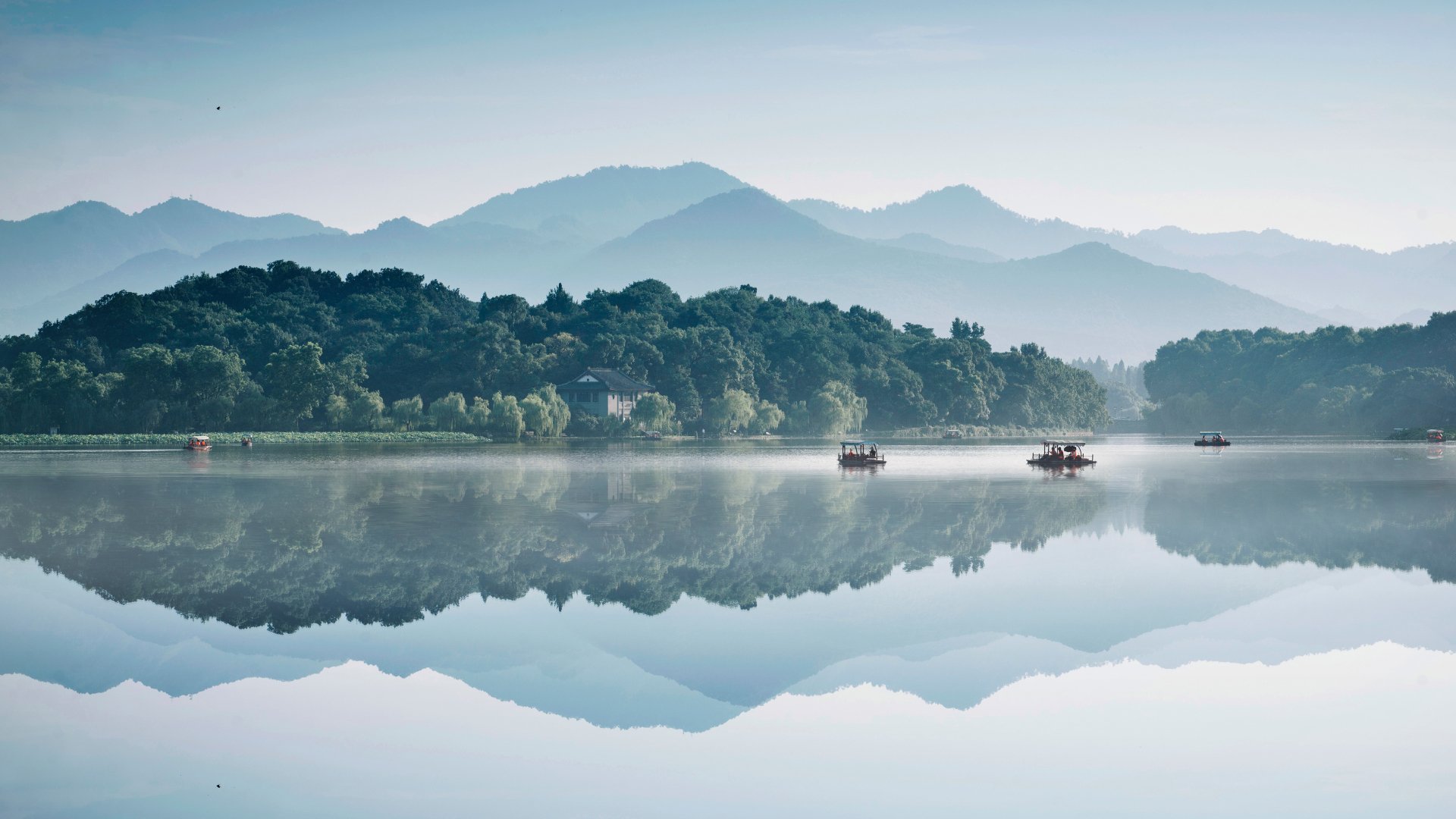 A serene 4K Ultra HD desktop wallpaper showcasing a calm lake with clear reflection of lush green trees and distant mountains under a pale sky.
