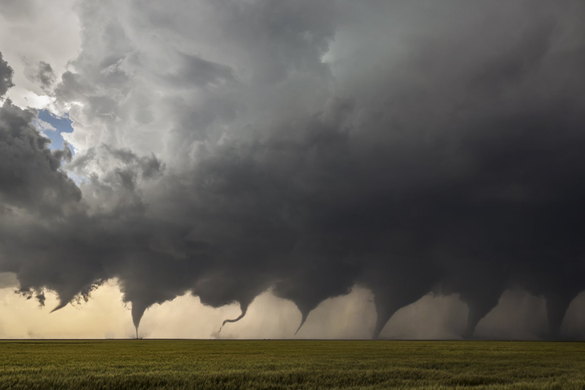 2K Quad HD PC desktop wallpaper: a wide prairie beneath dark storm clouds with several tornado funnels touching the ground, dramatic nature scene.