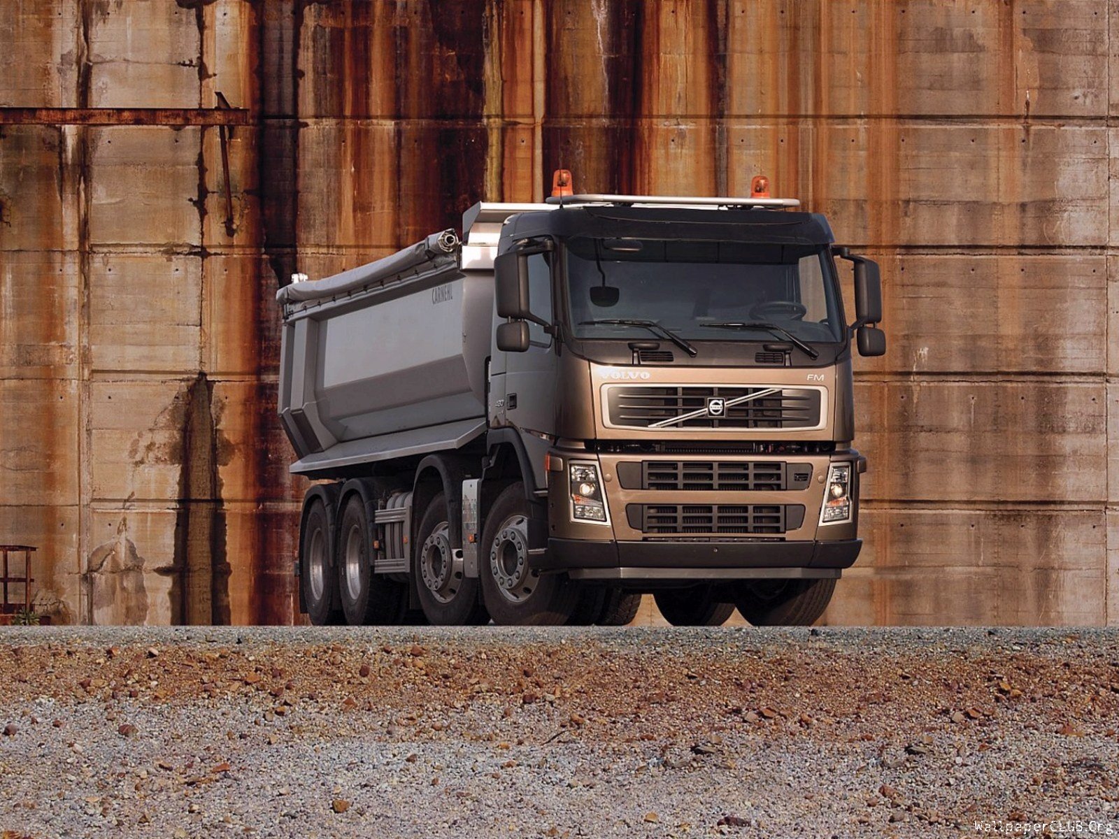 HD PC desktop wallpaper featuring a Volvo dump truck parked in front of a weathered industrial wall, highlighting rugged vehicle design and durability.