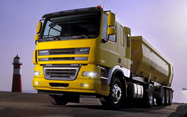 HD PC desktop wallpaper/background showing a yellow DAF heavy-duty truck (vehicle) parked by a lighthouse under a dusky purple sky.
