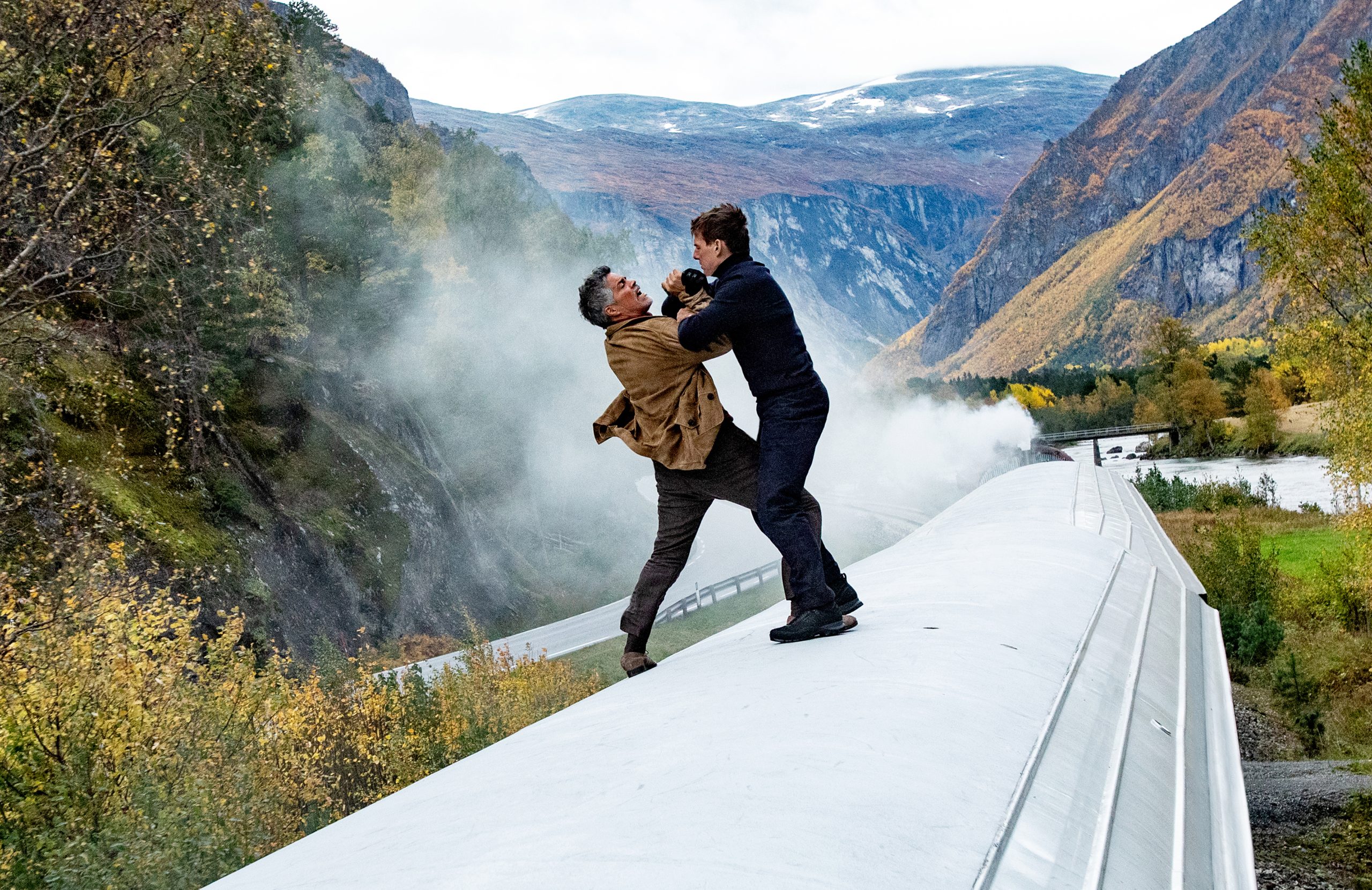 High-definition desktop wallpaper featuring an intense action scene from Mission: Impossible - Dead Reckoning Part One with two characters in a gripping confrontation atop a train, set against a stunning mountainous backdrop.