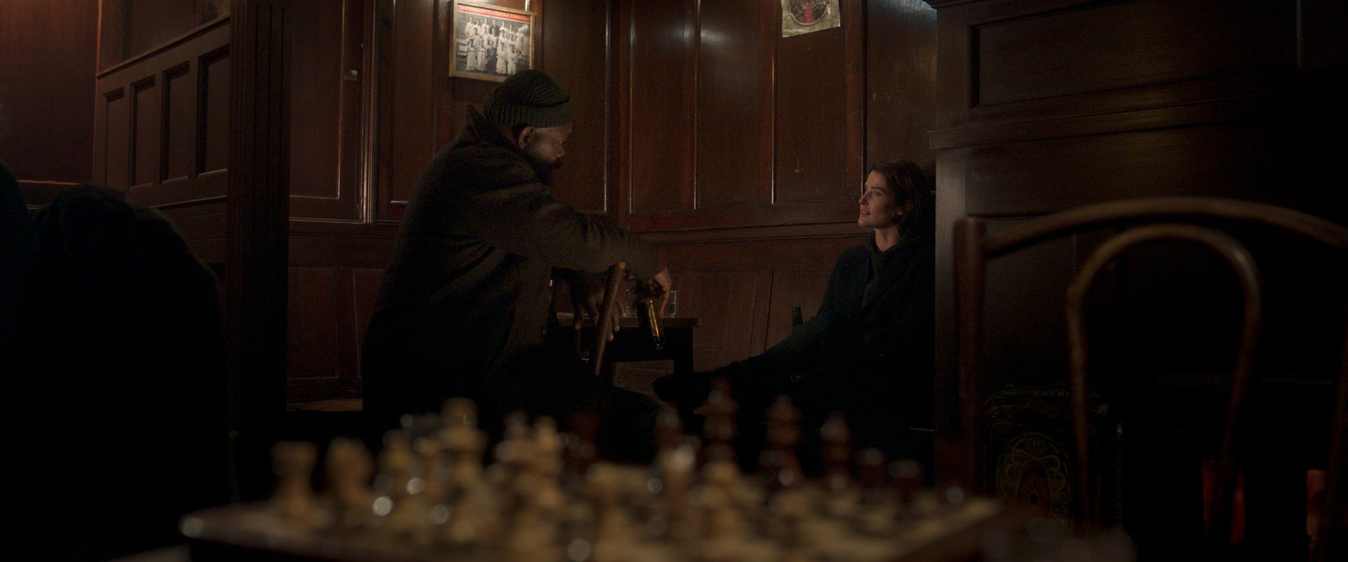 A scene from the TV show Secret Invasion, featuring two characters in a dimly lit space, with a chessboard in the foreground, creating an atmosphere of intrigue and tension.