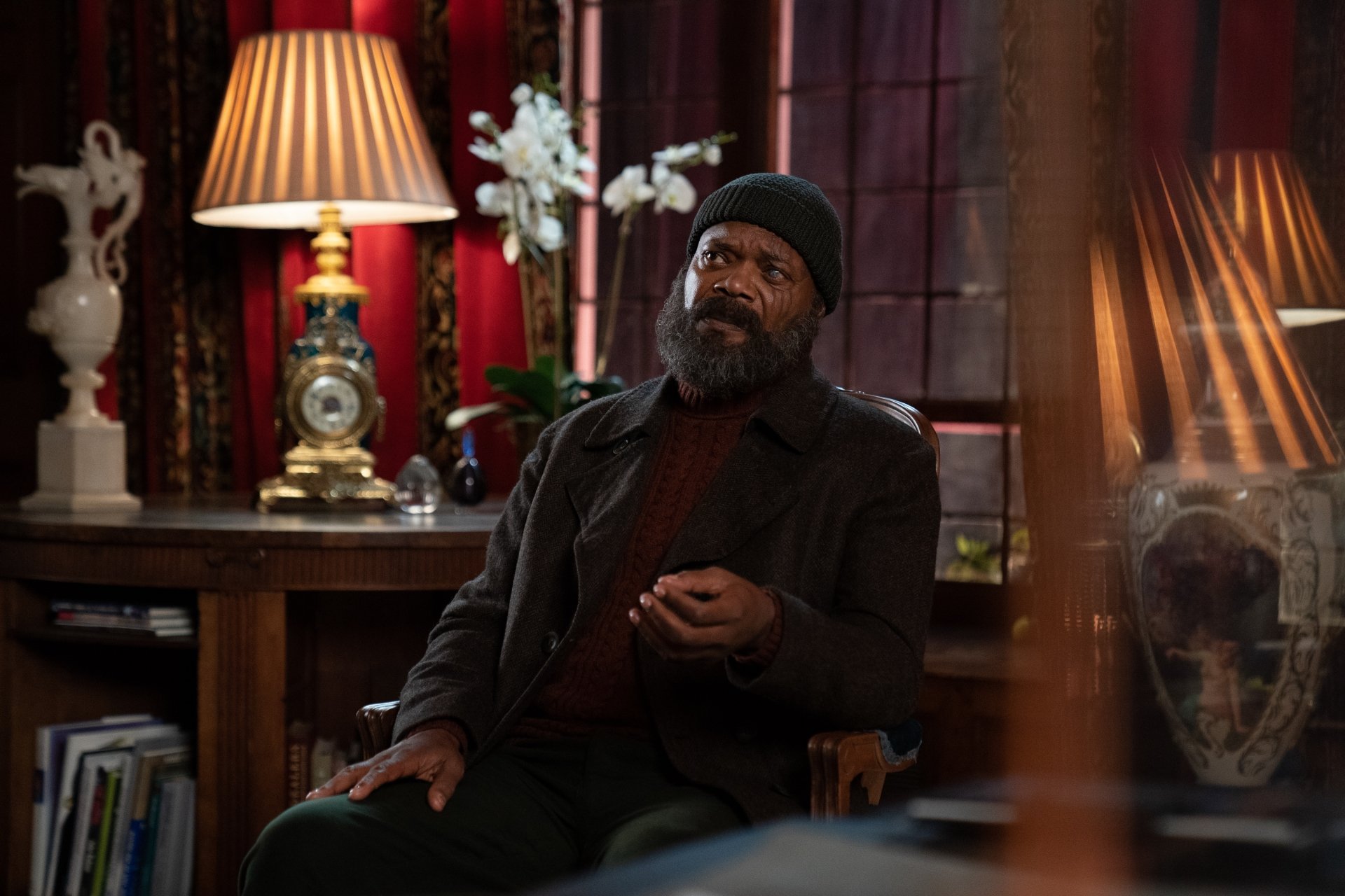 HD wallpaper of a scene from Secret Invasion featuring a character sitting thoughtfully in a warmly lit vintage room with elegant décor.