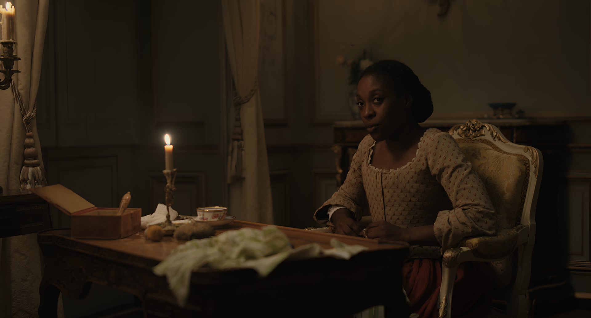 HD wallpaper featuring a thoughtful individual in historical attire sitting at a desk by candlelight, evoking a chevalier-era ambiance.
