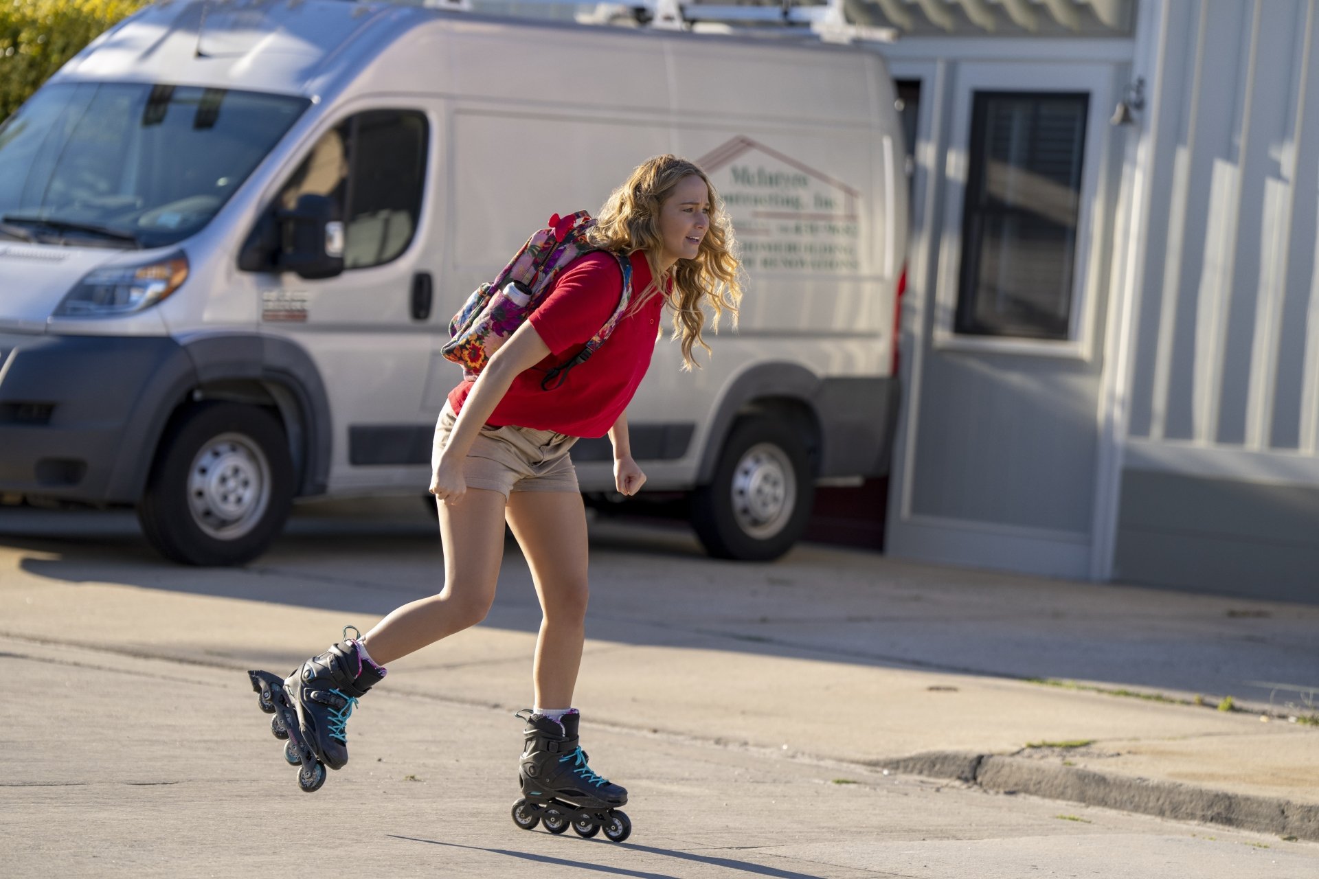 A young woman rollerblades down the street, wearing a red shirt and shorts, showcasing vibrant energy in this HD wallpaper from the movie No Hard Feelings.