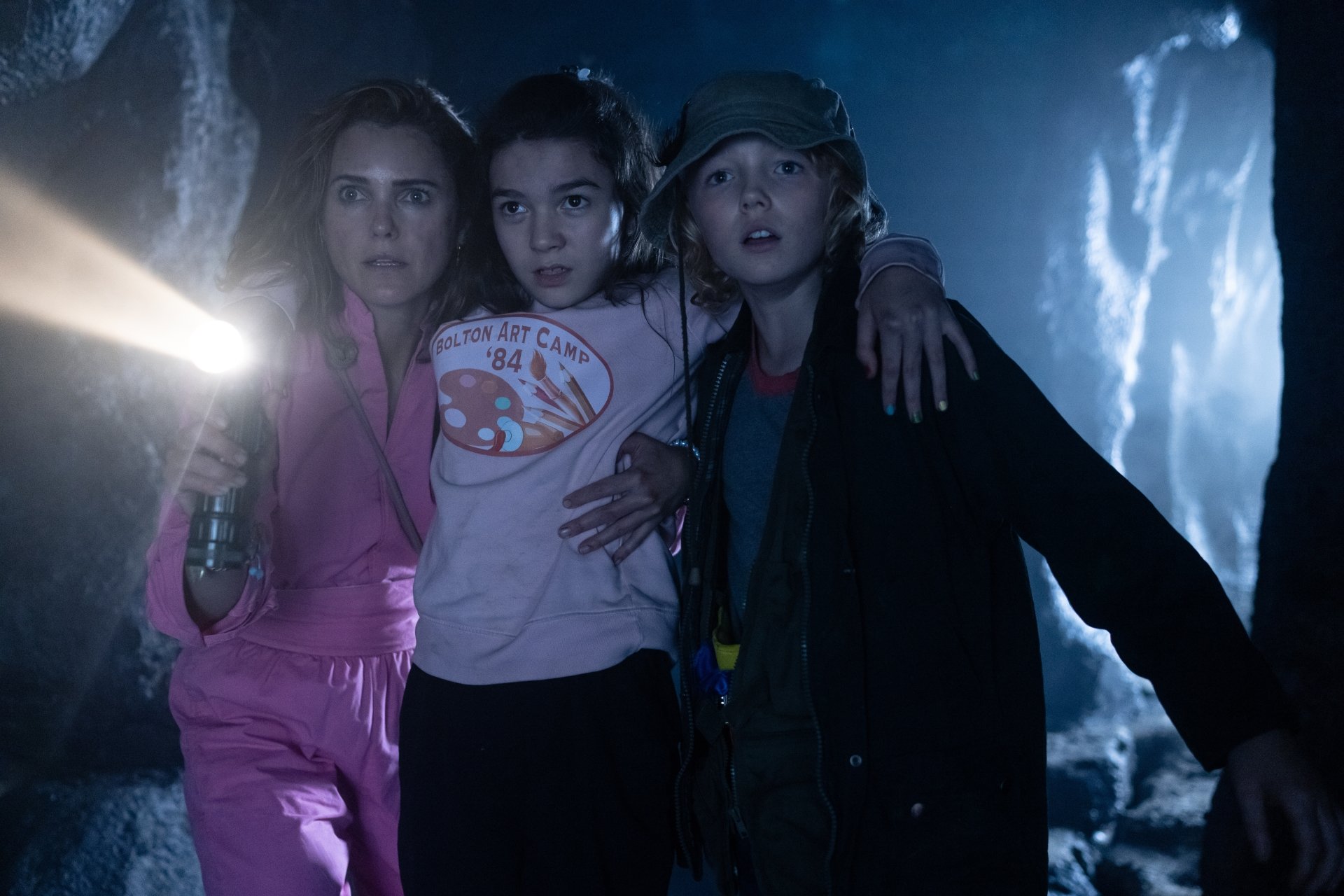 HD desktop wallpaper featuring three actors portraying frightened characters from the film 'Cocaine Bear', with a flashlight illuminating a dark, misty background suggestive of suspense.