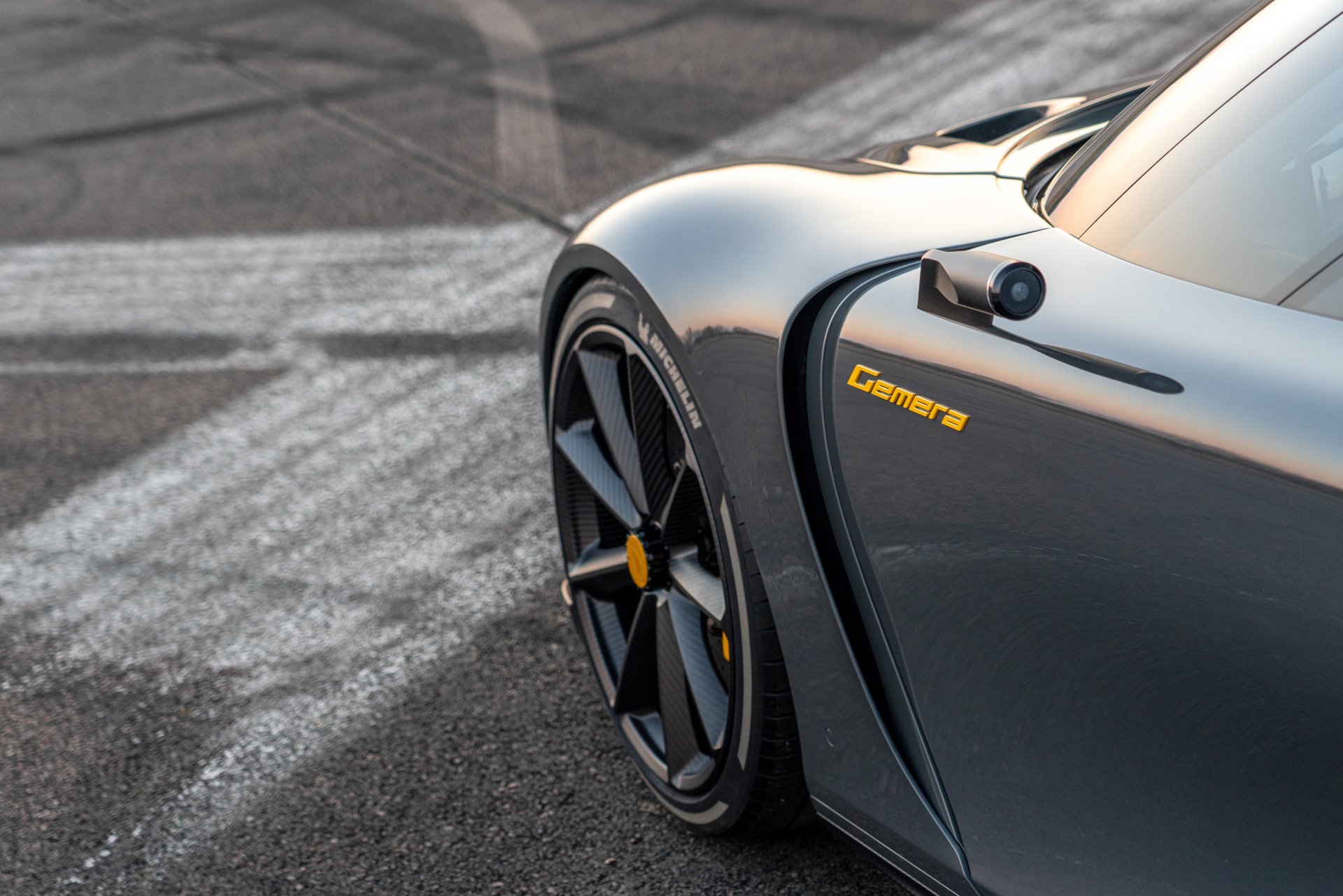 Close-up of a Koenigsegg Gemera showcasing its sleek design and distinctive wheel, set against an asphalt background marked by tire tracks. An impressive HD desktop wallpaper.