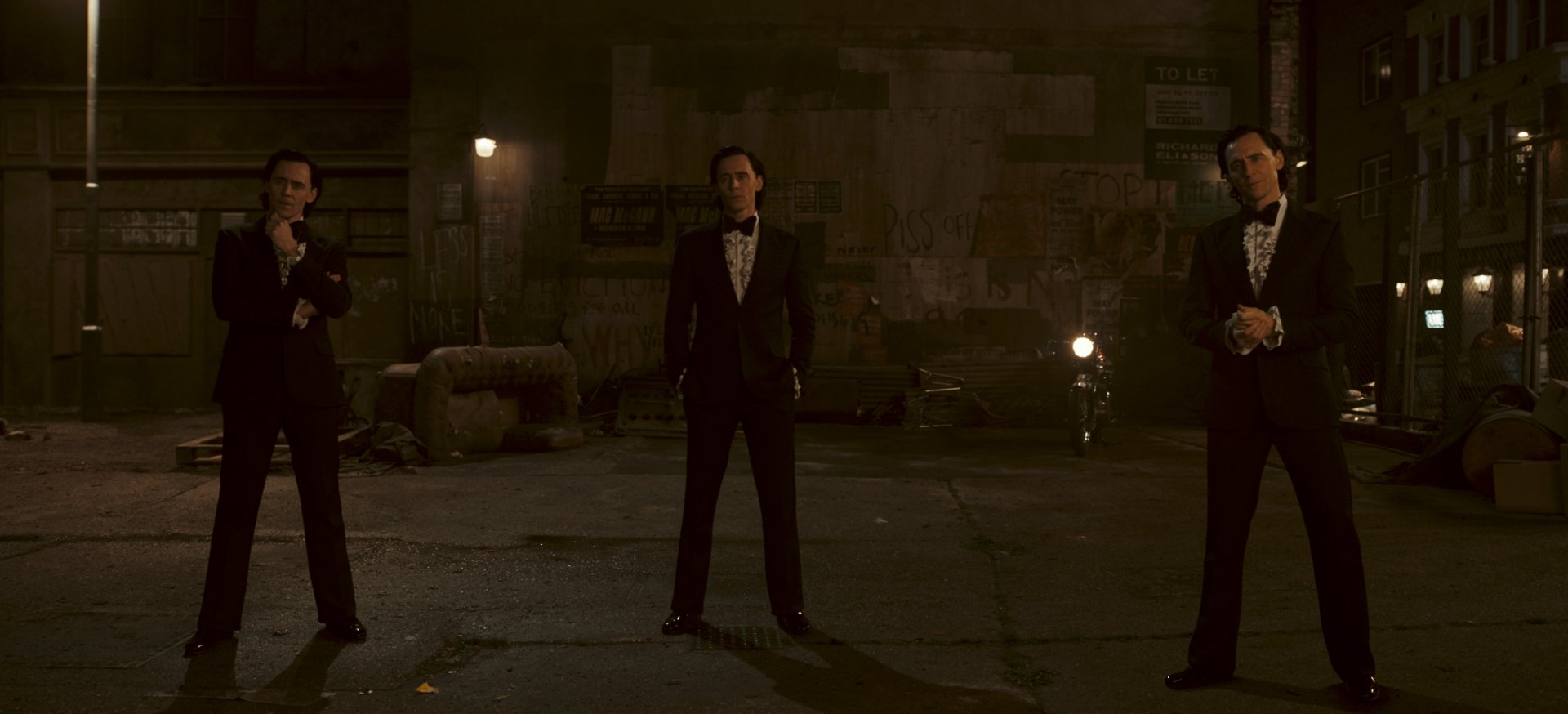 Three men in suits standing in a dimly lit alleyway from the Loki Season 2 series - a high-definition desktop wallpaper.