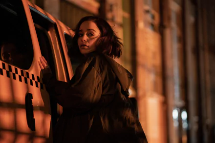 A woman in a dark jacket leans against a van, illuminated by warm orange tones. This striking image is a HD wallpaper inspired by the TV show Secret Invasion.