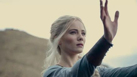 HD wallpaper featuring Freya Allan in The Witcher TV show, showcased in a thoughtful pose with her hand extended against a soft, hilly backdrop.