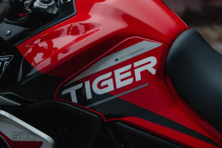 Close-up view of the red fuel tank on a Triumph Tiger 900 motorcycle, showcasing the Tiger emblem and 900 GT Aragón decal, suitable as a HD desktop wallpaper.