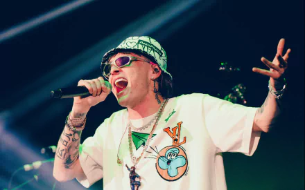 HD desktop wallpaper of a performer singing passionately on stage, tagged with Peso Pluma, with vibrant lighting in the background.