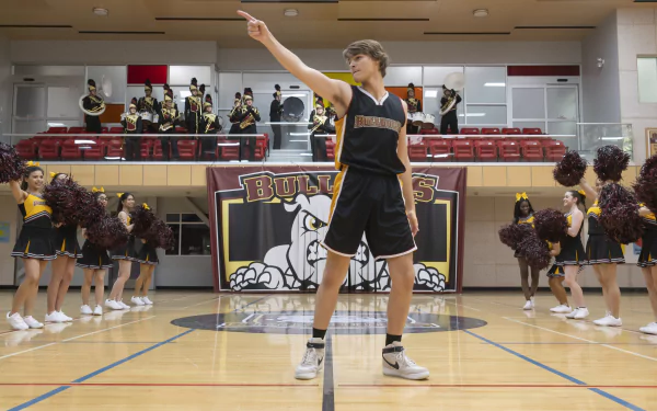 A high-resolution desktop wallpaper featuring a moment from Prom Pact with a basketball player confidently pointing in the gym while cheerleaders and a band perform in the background.
