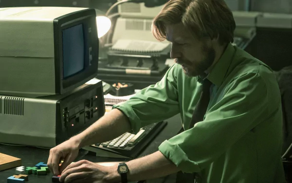 A scene from the movie Tetris features a man in a green shirt focused on arranging colorful puzzle pieces near vintage computers, creating a nostalgic atmosphere for this HD wallpaper.