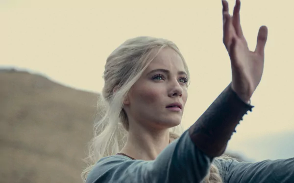 HD wallpaper featuring Freya Allan in The Witcher TV show, showcased in a thoughtful pose with her hand extended against a soft, hilly backdrop.