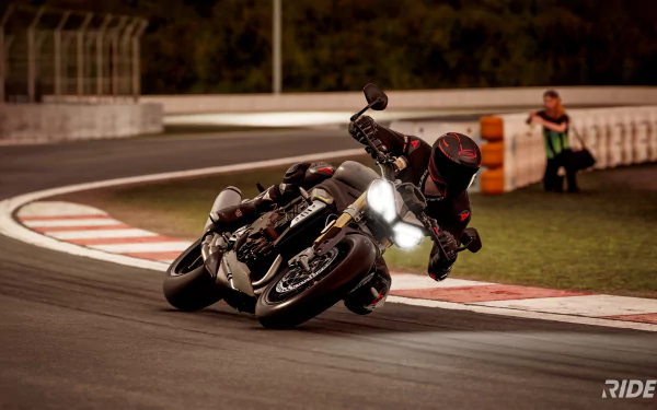 HD desktop wallpaper from the video game Ride 5 featuring a motorcyclist sharply cornering on a racetrack, demonstrating dynamic motion and detailed graphics.