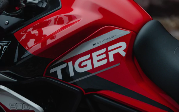 Close-up view of the red fuel tank on a Triumph Tiger 900 motorcycle, showcasing the Tiger emblem and 900 GT Aragón decal, suitable as a HD desktop wallpaper.