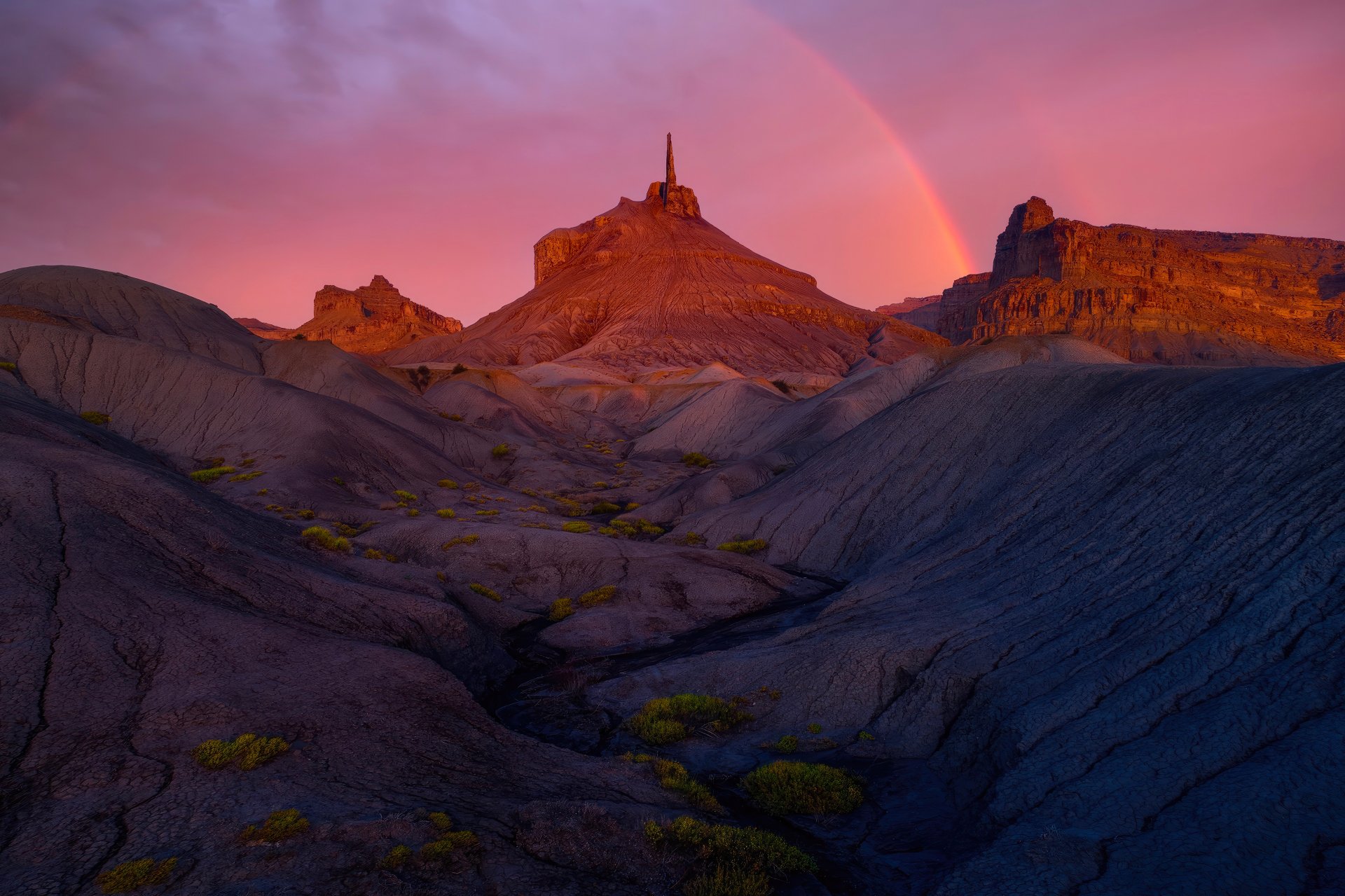 4K Ultra HD PC desktop wallpaper featuring a vibrant sunset over rugged rock formations with a faint rainbow arching across the colorful sky.