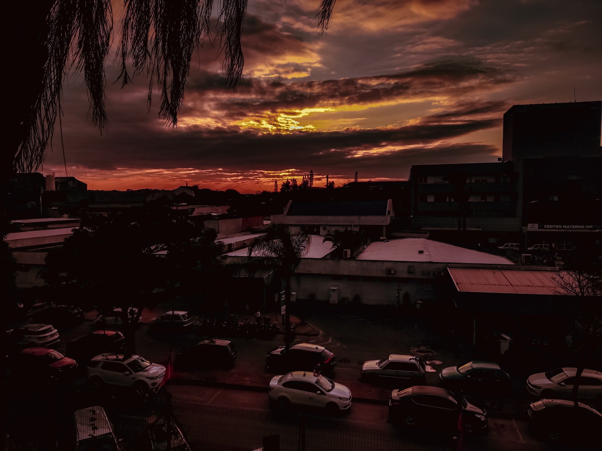 4K Ultra HD PC desktop wallpaper: urban sunset with a dramatic cloud-filled sky casting orange light over rooftops, buildings and parked cars.