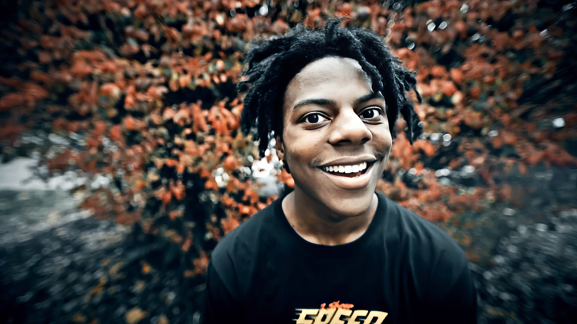 A high-definition background featuring IShowSpeed, smiling widely against a backdrop of vibrant orange foliage, creating an energetic and engaging atmosphere.