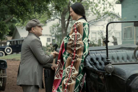HD desktop wallpaper featuring a scene from Killers of the Flower Moon with two characters in period costume, standing beside a vintage car.