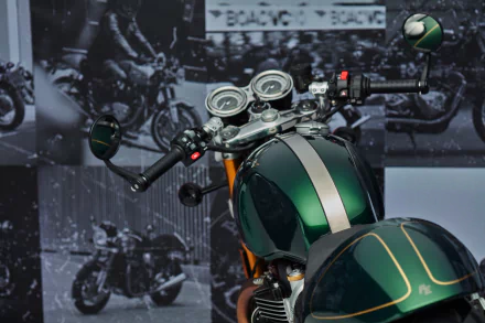 Close-up view of a Triumph Thruxton Final Edition motorcycle as an HD desktop wallpaper, showcasing its sleek tank design with classic racing stripes against a backdrop of vintage racing images.
